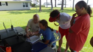 Under the watchful eye of Bill and her father the young field day participant gives the running station her station information for their log book. 